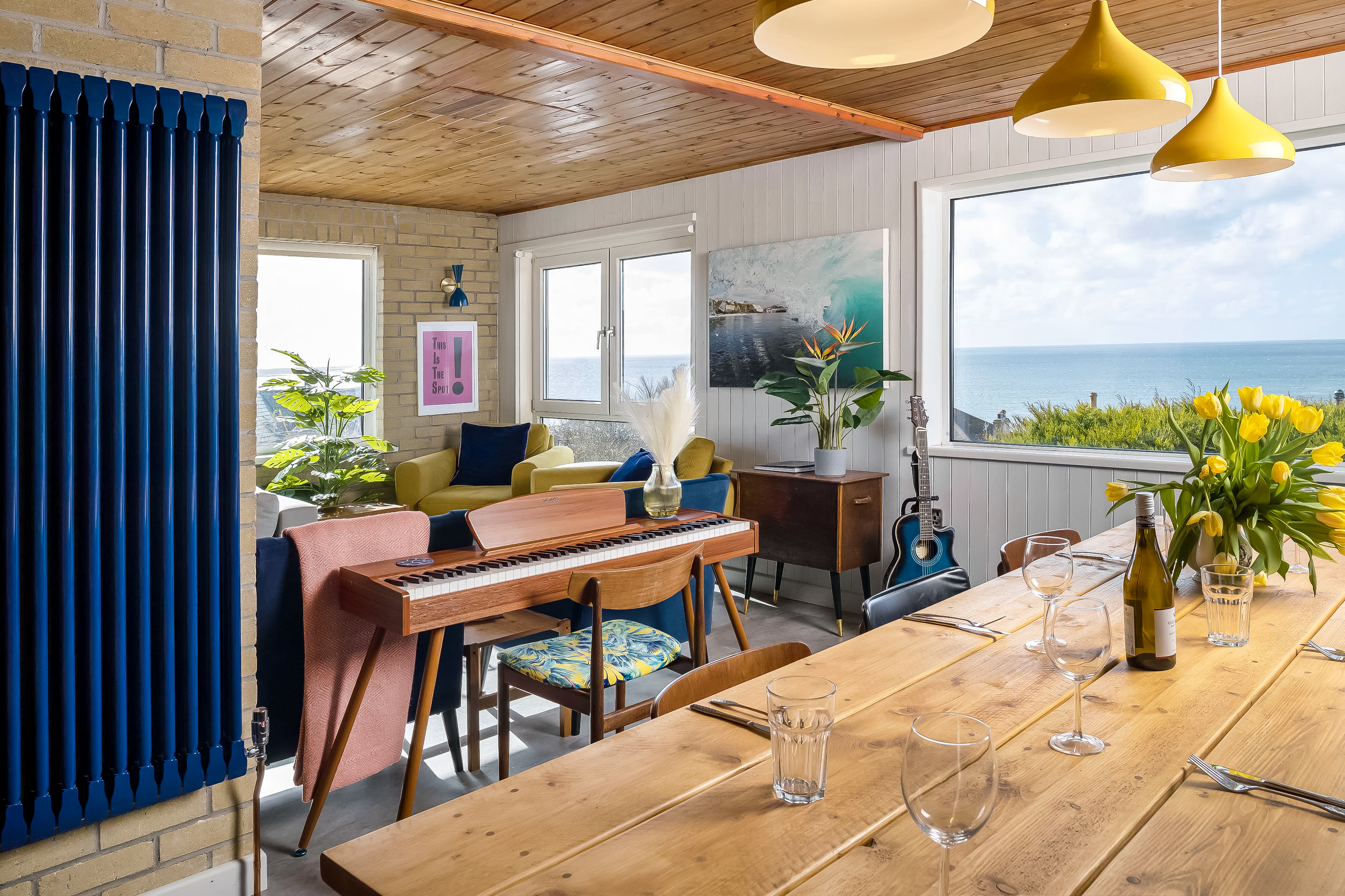 Open plan living and dining area with sea views, piano, and mustard pendant lights